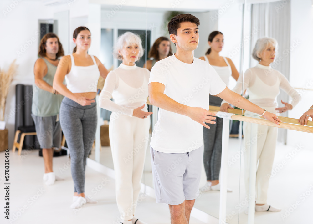 Fototapeta premium Group of dancers doing exercises using ballet barre in a modern fitness studio.