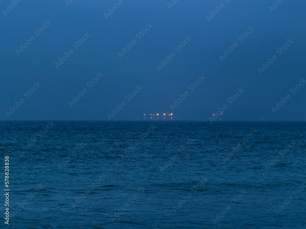 Deep blue water and Bokeh lights over the sea on the horizon. Ocean evening landscape. Odesa, Ukraine