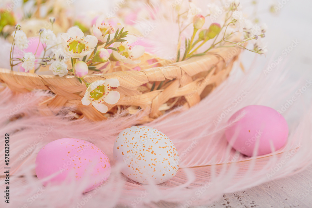 Easter candy chocolate eggs and almond sweets lying in a bird's nest decorated with flowers and feathers on white wooden background. Happy Easter concept.