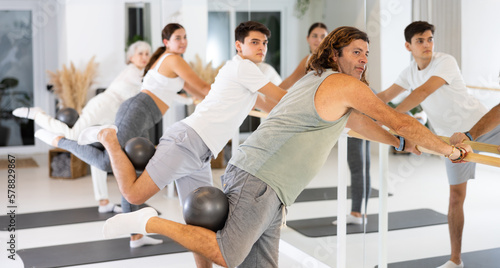 Fototapeta Naklejka Na Ścianę i Meble -  Sporty energetic males and females doing exercises with pilates ball during group training at gym. Fitness concept.