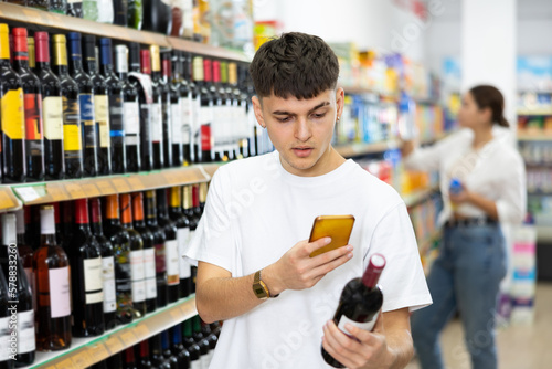 Young man looking up wine on internet in supermarket
