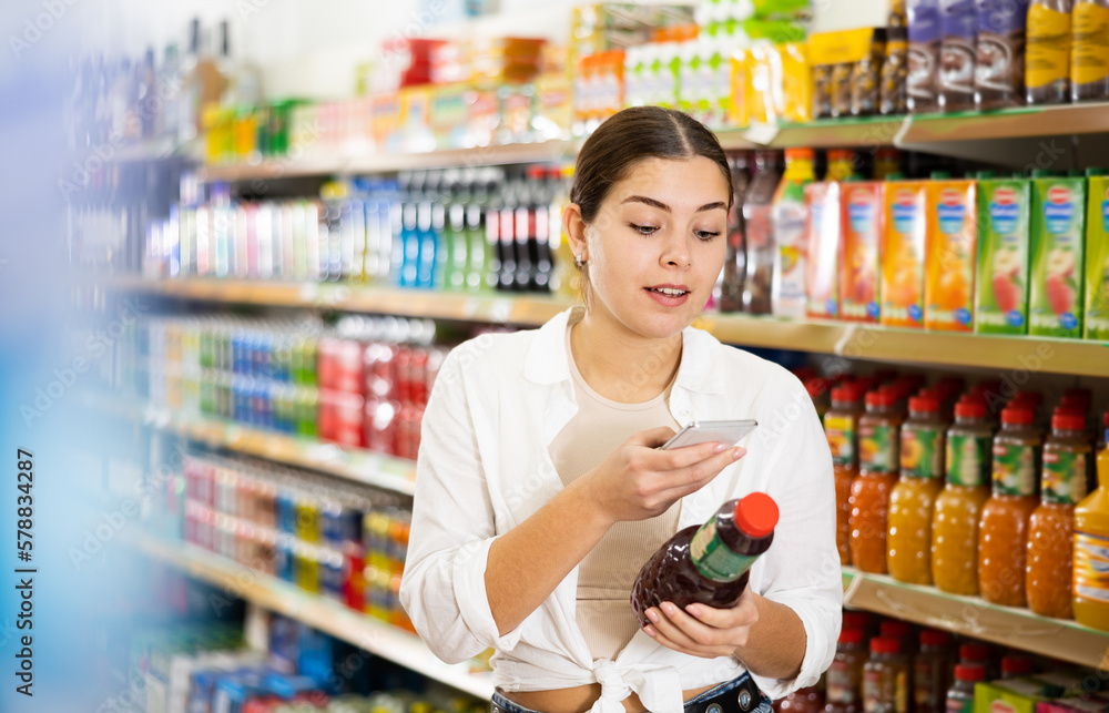 Young woman looking up contents of juice on internet in supermarket