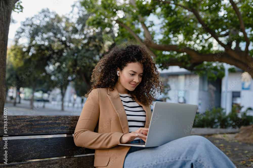pretty curly woman sitting in city street in stylish jacket, working remote job on laptop pretty curly woman sitting in city street in stylish jacket, working remote job on laptop