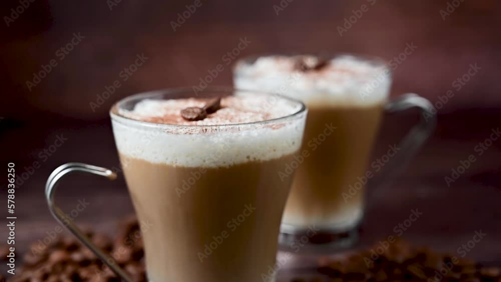 Two cups of coffee hot drinks, with milk foam in glass cups, over wooden background Two cups of coffee hot drinks, with milk foam in glass cups, over wooden background