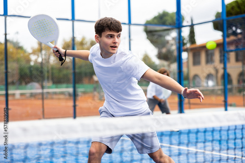 Young man in sportswear playing padel tennis match during training on court
