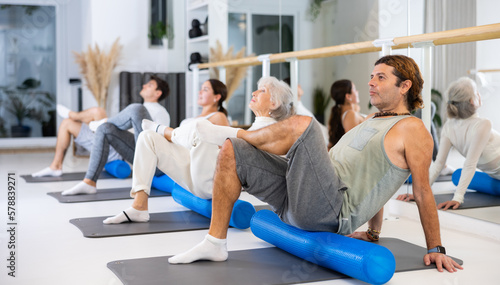 Willing middle-aged man engaging in pilates training with roller in gym room during training session