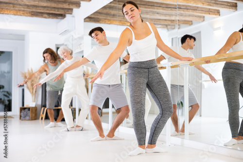 Gracile young woman engaging in ballet at ballet barre in training hall during workout session