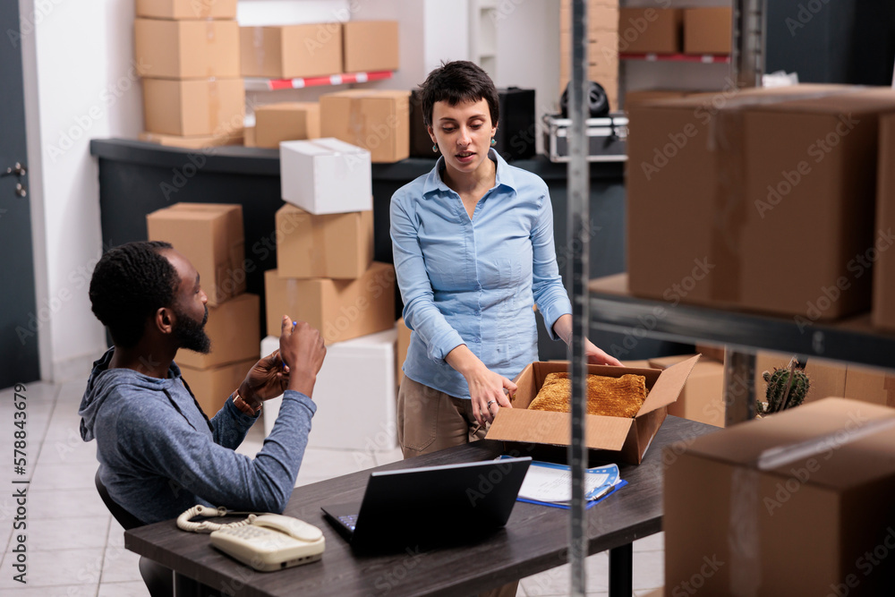 Warehouse manager preparing packages putting client order in cardboard box while discussing shipping detalies with supervisor. Diverse team working in storehouse delivery department Warehouse manager preparing packages putting client order in cardboard box while discussing shipping detalies with supervisor. Diverse team working in storehouse delivery department