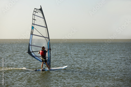 Windsurfer against the backdrop of the setting sun, on calm water, goes calmly along the sea, active recreation, copyspace.