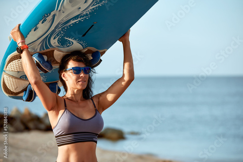 Photography Sexy middle aged brunette with a surfboard in the setting sun holds a surfboard on her head, surfing as a lifestyle, waiting for the waves