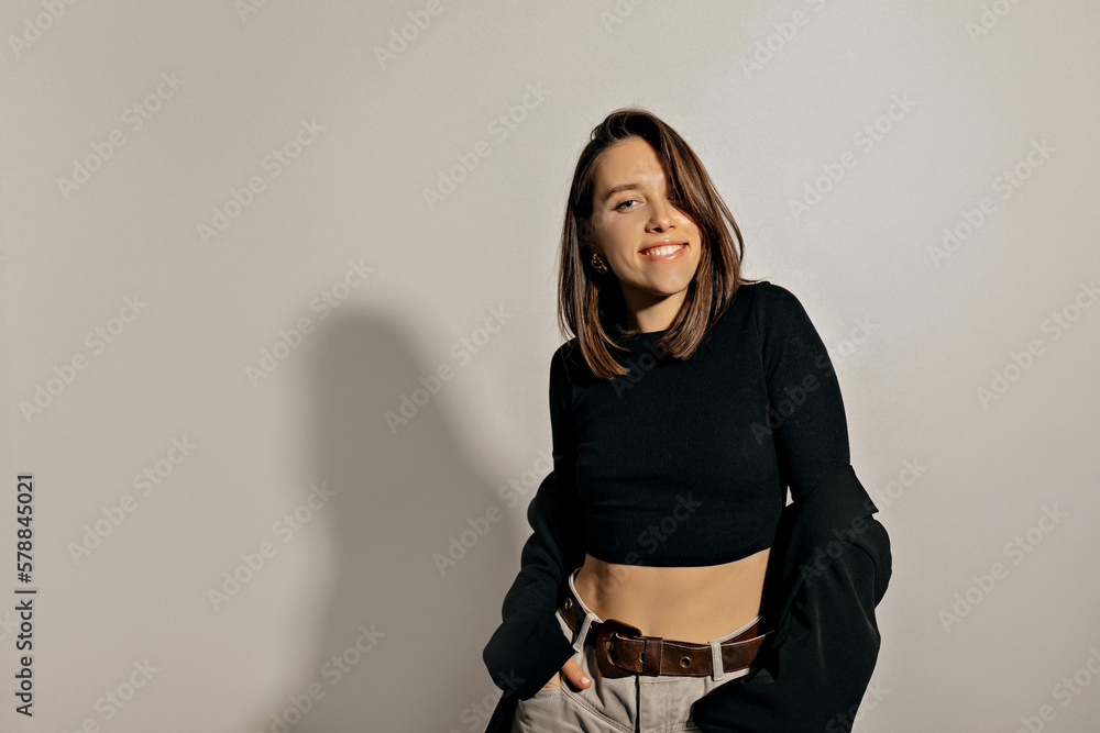 Studio photo of attractive smiling charming girls with wonderful smile and short hairstyle is wearing black top, jacket and jeans is smiling to camera over isolated background Studio photo of attractive smiling charming girls with wonderful smile and short hairstyle is wearing black top, jacket and jeans is smiling to camera over isolated background