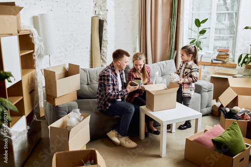 Putting things on place. Young happy family, man, woman and kid moving into new flat, apartment with many cardboard boxes. Concept of moving houses, real estate, family, new life © master1305