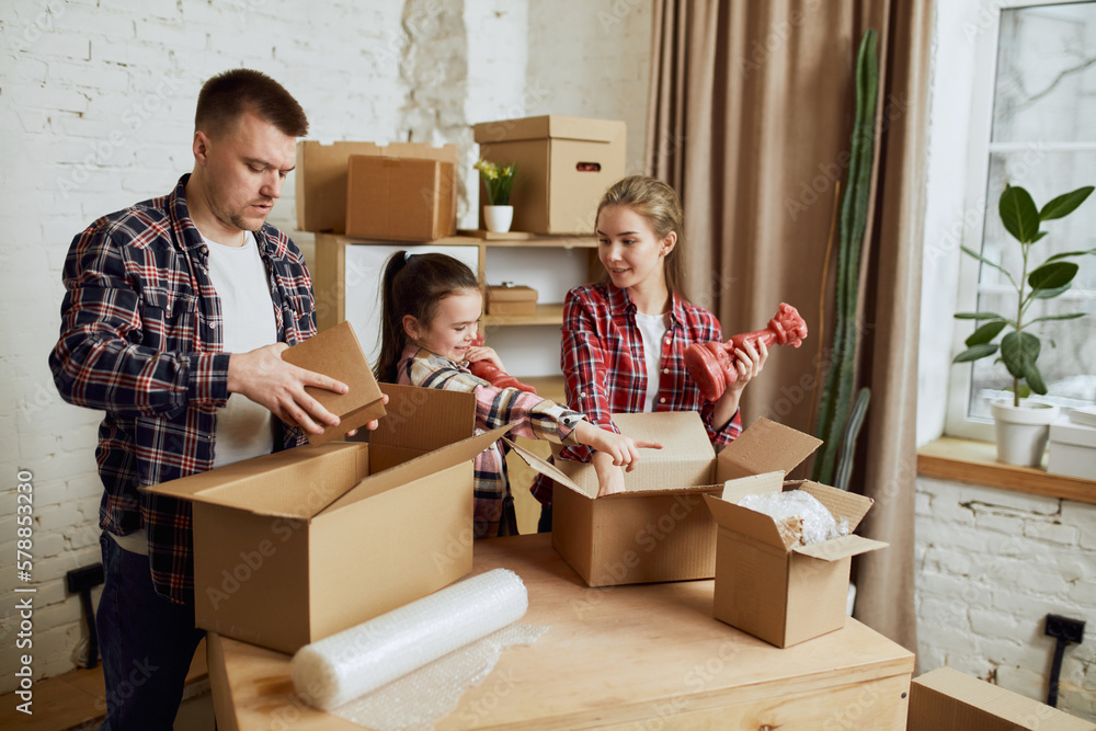 Young happy family, man, woman and kid moving into new flat, apartment with many cardboard boxes filled with stuffs and clothes. Concept of moving houses, real estate, family, new life Young happy family, man, woman and kid moving into new flat, apartment with many cardboard boxes filled with stuffs and clothes. Concept of moving houses, real estate, family, new life