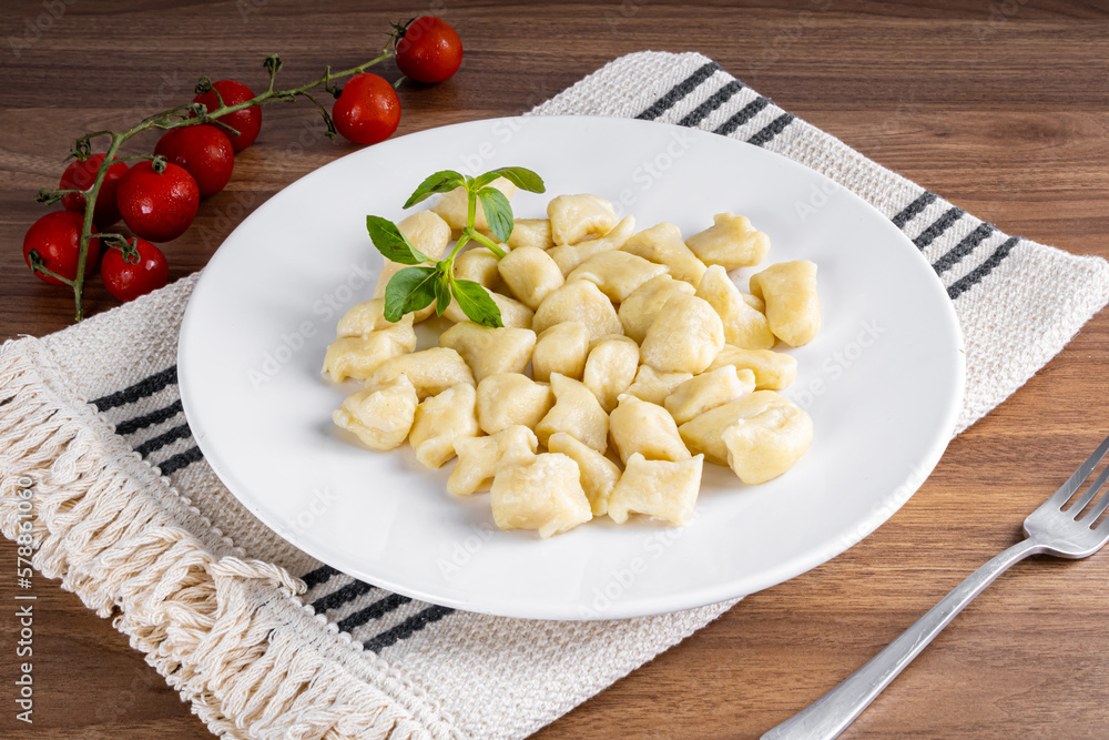 BAKED GNOCC IN A WHITE PLATE ON A WOODEN BACKGROUND. DETAIL OF BASIL AND SMALL TOMATOES.