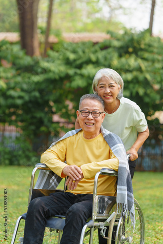 Elderly couple husband and wife happy asian people giving love and care Wheelchair in the park relaxing in spring, relaxing and walking outside at the park. © NanSan
