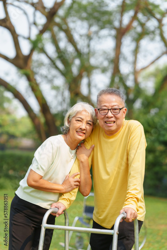 Elderly Asian couple and wife caring for their family enjoying retirement together in park. Old Caregiver people take close care while using walking cane stick. © NanSan
