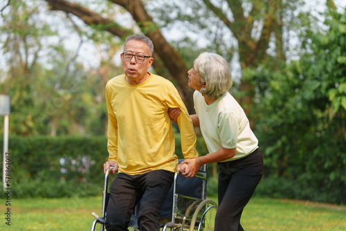 Elderly Asian couple and wife caring for their family enjoying retirement together in park. Old Caregiver people take close care while using walking cane stick.