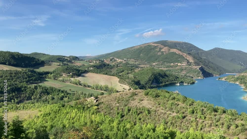Left-to-right panning view from Chiesa di San Paolo at Lago di Fiastra (Lake Fiastra) and its finely-toned azure waters enclosed by an artificial dam amongst Marche hills, vegetation and the Sibillini Left-to-right panning view from Chiesa di San Paolo at Lago di Fiastra (Lake Fiastra) and its finely-toned azure waters enclosed by an artificial dam amongst Marche hills, vegetation and the Sibillini