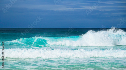 Low angle view of turquoise ocean waves breaking near beach with blue sky above