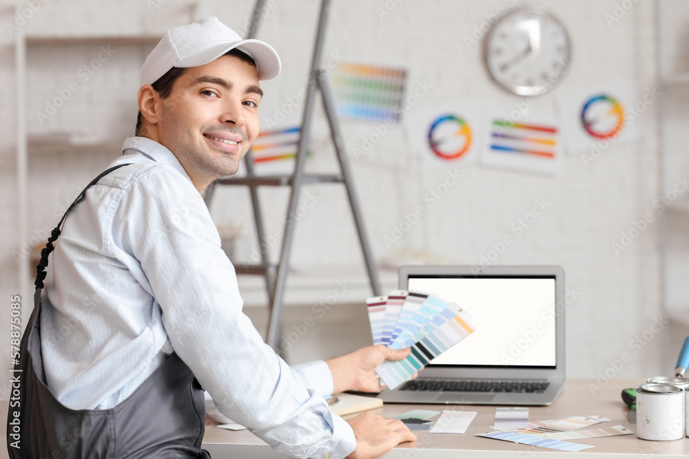 Male painter with color palettes sitting at table in room Male painter with color palettes sitting at table in room