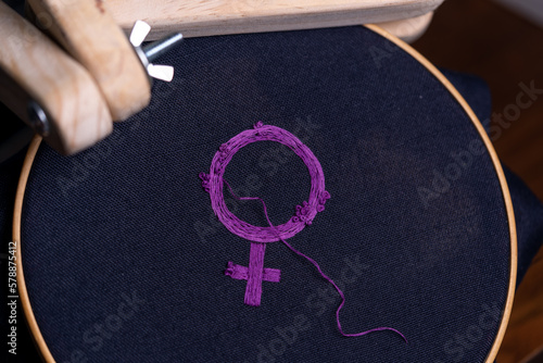 símbolo feminista bordado recién terminado con hilo suelto, sobre bastidor redondo de madera y sostenido por portabastidor