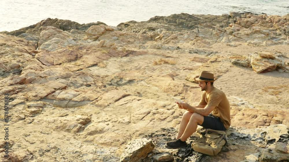 Caucasian man traveler writing journey memories in diary book on coastline hill at sunset. Handsome guy enjoy outdoor lifestyle hiking on island mountain on summer vacation. Solo travel concept. Caucasian man traveler writing journey memories in diary book on coastline hill at sunset. Handsome guy enjoy outdoor lifestyle hiking on island mountain on summer vacation. Solo travel concept.
