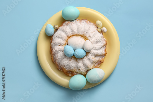 Plate with sweet Easter cake and painted eggs on color background
