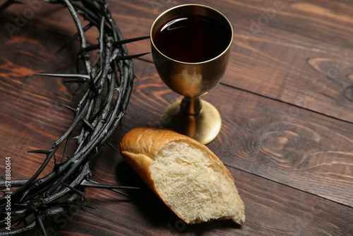 Fotografía Crown of thorns with cup of wine and bread on wooden background, closeup