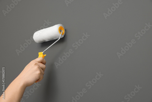 Worker using roller to paint wall with grey dye, closeup. Space for text