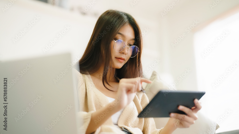 Young asian woman wearing glasses and using tablet while seated on couch at home Young asian woman wearing glasses and using tablet while seated on couch at home