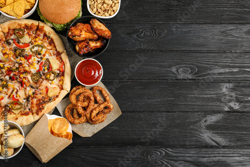 Wall Mural Pizza, onion rings and other fast food on black wooden table, flat lay with spac