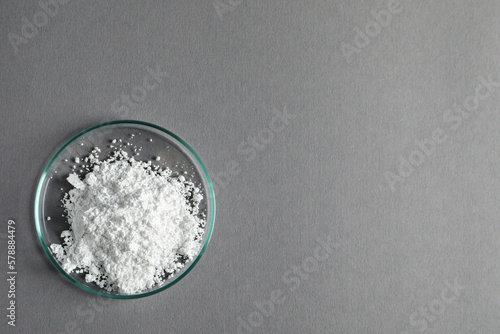 Petri dish with calcium carbonate powder on grey table, top view. Space for text