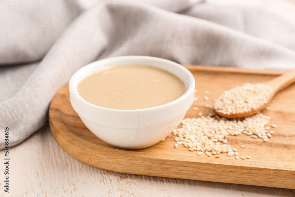 Board with bowl of tasty tahini and sesame seeds on light wooden table, closeup Board with bowl of tasty tahini and sesame seeds on light wooden table, closeup