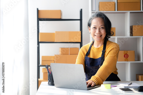 Senior woman business owner selling online products, she is checking orders from customers, sending goods through a courier company, Senior woman concept opening an online store. © kamiphotos