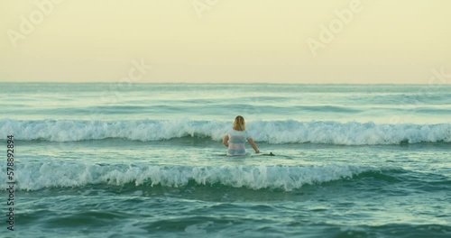 Blonde surfer with board enter breaking green Costa Rica waves in sunrise glow
