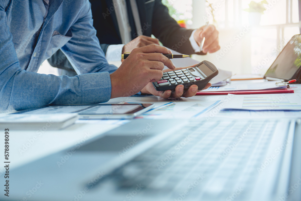 Fototapeta premium Businessmen analyzing investment graphs, brainstorming meeting and discussing plans in conference room. Using graph sheets, laptops and calculators. business and investment ideas