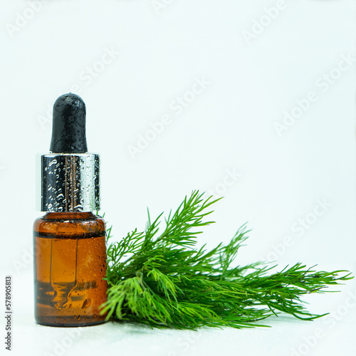 Dill essential oil in a glass bottle and a bunch of fresh dill grass on a white table. Anethum graveolens extract. The concept of healthy nutrition, herbal medicine or naturopathy. Selective focus.