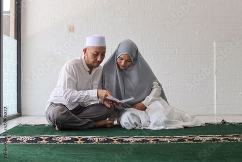 Muslim couple reading Quran together, husband teaching his wife reciting Koran during a ramadan feast at the mosque photo