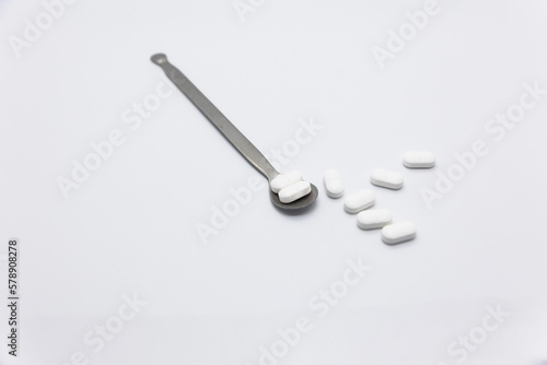 Painkillers on a white refined silver medicine spoon on a white background © HYUNGGYU