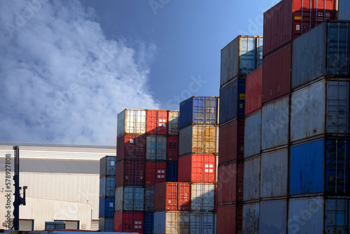 Stacks of cargo containers, import/export ships in port harbour, industrial cargo shipping, container logistics, maritime transport distribution yard.