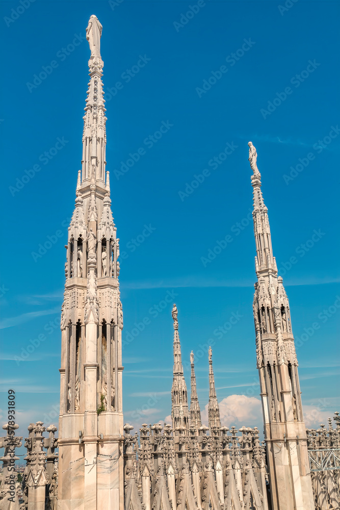 Statues atop the spires of the Duomo di Milano, the Milan cathedra; in the crown of spires each topped by a unique statue intricate stone sculptures, spires, gargoyles and statues is most recognizable Statues atop the spires of the Duomo di Milano, the Milan cathedra; in the crown of spires each topped by a unique statue intricate stone sculptures, spires, gargoyles and statues is most recognizable