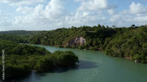 Dolly out aerial drone shot of the large winding tropical Gramame river with turquoise water surrounded by foliage and cliffs near the tropical beach capital city of Joao Pessoa in Paraiba, Brazil. photo