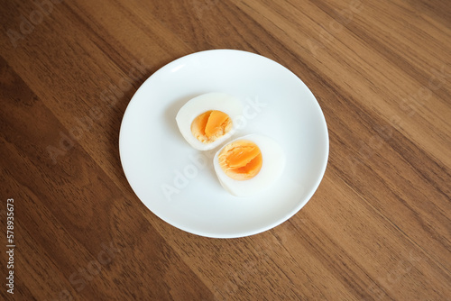 Sliced Boiled egg in white ceramic plate on wooden table.