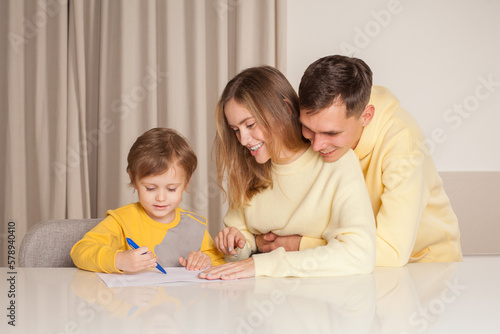 Adorable family, cute parents in yellow clothes with their child son drawing