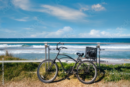 A bicycle against the parapet on the walking path at North Cronulla Beach in Sydney, NSW, Australia. Seascape background on a sunny day with calm waves and blue skies.