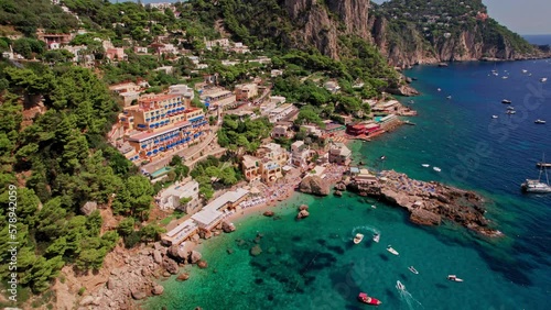 A cinematic aerial shot of the beautiful cliffs and beach landscape of Marina Piccola on the island of Capri, a popular tourist destination along the Amalfi Coast in the Bay of Naples in Italy. photo