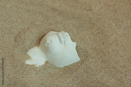 A piece of plaster face sculpture in the sand.