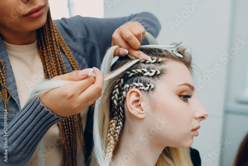 Hairstylist braided afro braids dreadlocks kanekalon pigtails hair of female client in barber salon.