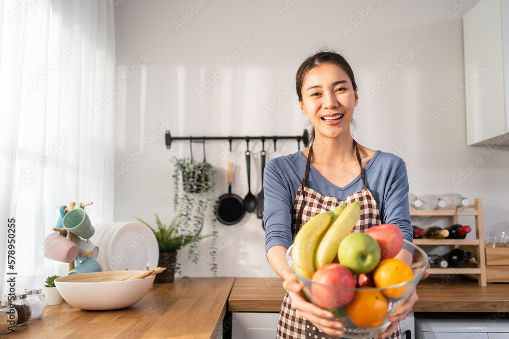 Portrait of Asian young woman hold a bowl of fruits and look at camera. 