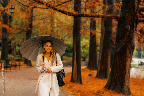 Woman with umbrella taking a walk in autumn park on rainy day  orange and red leaves have fallen on the ground